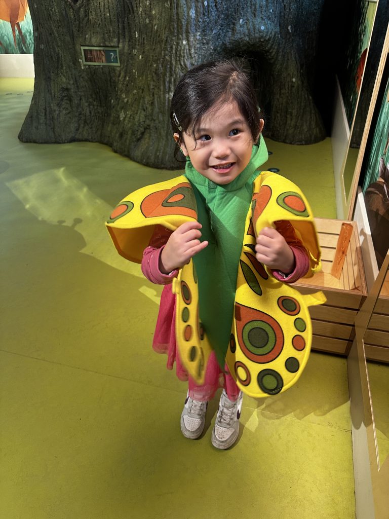 An adorable 4-year-old girl in a vibrant butterfly costume, enjoying one of the top things to do with kids in Edinburgh - exploring the National Museum of Scotland.