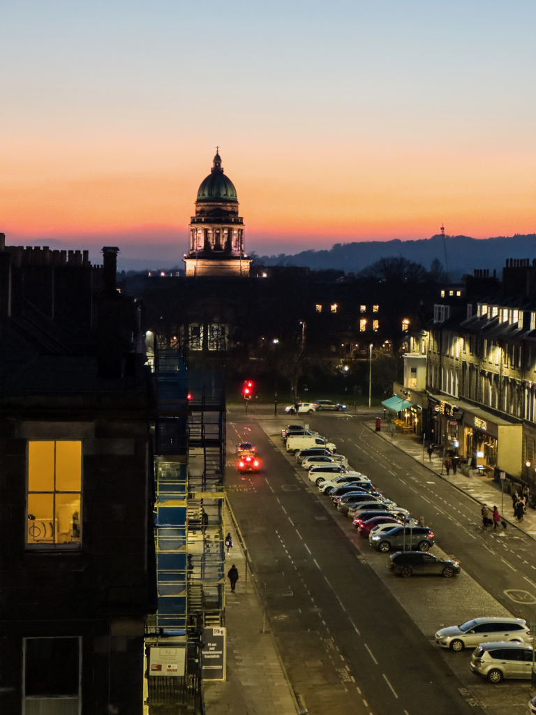 A stunning view of a building in Edinburgh with a prominent dome structure, set against the backdrop of a beautiful sunset.