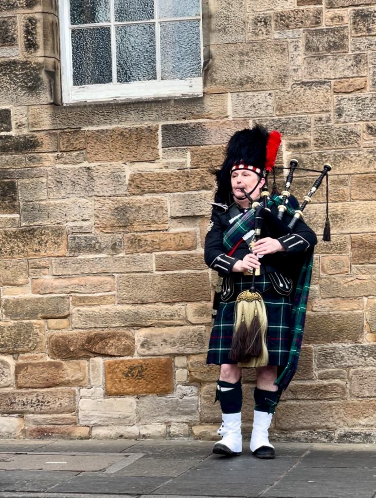 A Scotsman dressed in traditional attire playing the bagpipes with passion and skill along the vibrant streets of Edinburgh.
