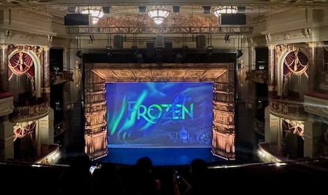 Audience perspective of a theatre stage with 'Frozen' displayed on the screen, highlighting one of the best London attractions for families.
