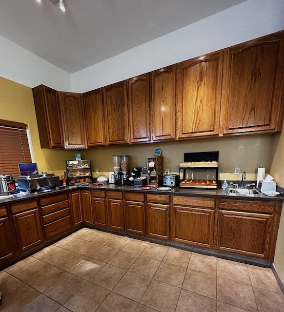 A breakfast area with wooden cabinets and a countertop displaying various breakfast items, including a toaster, coffee maker, juice dispenser, and cereal containers.