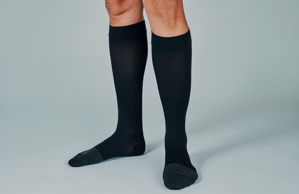 Person wearing long black compression socks with dark gray toes, standing on a light background.