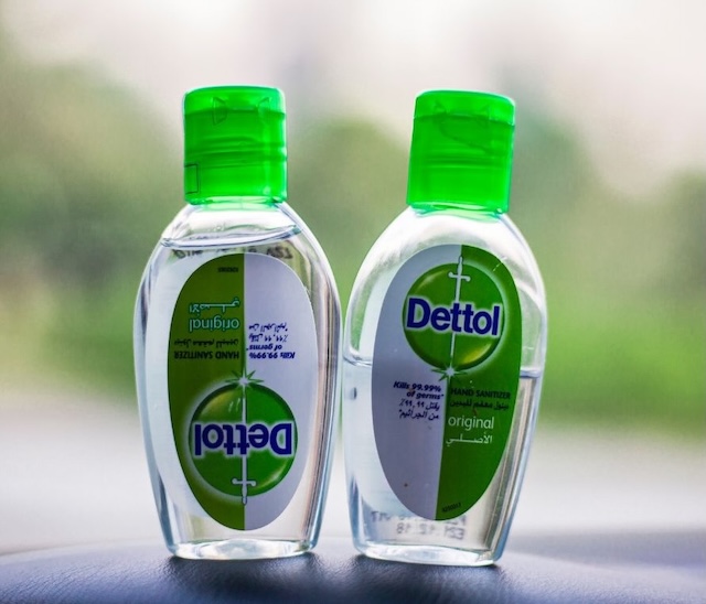 Two small clear bottles of Dettol original hand sanitizer with green caps, one standing upright and the other upside down.