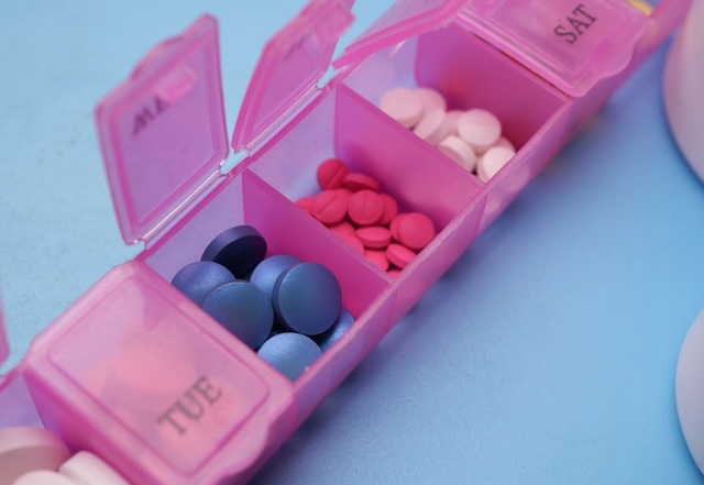 Close-up of a pink weekly pill organizer with labeled compartments for each day, filled with various colorful tablets and supplements. A compact and practical travel stocking stuffer for staying on track with medications or vitamins.