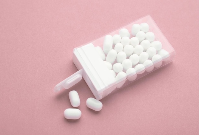 Clear plastic container filled with white mints or gum, partially opened with a few pieces spilled out. Fresh breath essentials are easy travel stocking stuffers.