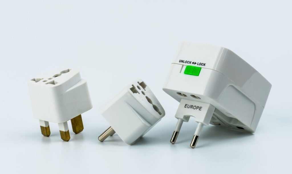 Group of three white international travel plug adapters, including one labeled for Europe with a sliding lock feature. Handy and essential travel stocking stuffers for globetrotters