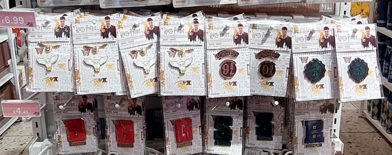 Close-up of Harry Potter-themed badge pins on display, featuring designs like Hedwig, Platform 9 ¾, house crests, and initial letters for Gryffindor, Slytherin, Ravenclaw, and Hufflepuff. These small items are ideal as themed Harry Potter stocking stuffers for fans who love collecting memorabilia.