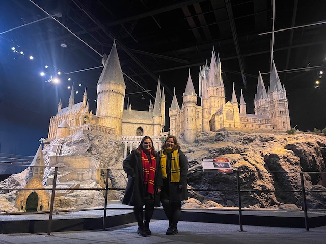 Two visitors wearing Hogwarts house scarves stand in front of the detailed Hogwarts Castle model at the Harry Potter Studio Tour. The iconic film set is one of the highlights visitors see at Warner Bros Studios - The Making of Harry Potter.
